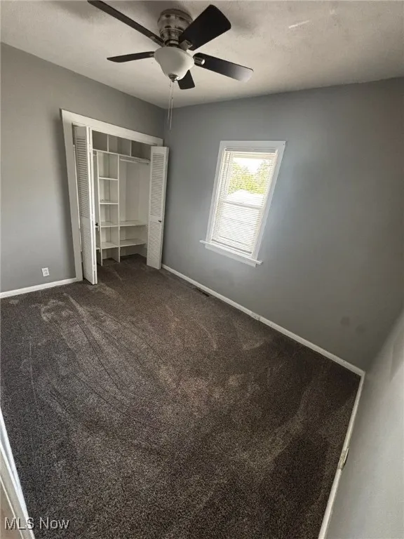 Unfurnished bedroom featuring dark colored carpet, a closet, and ceiling fan