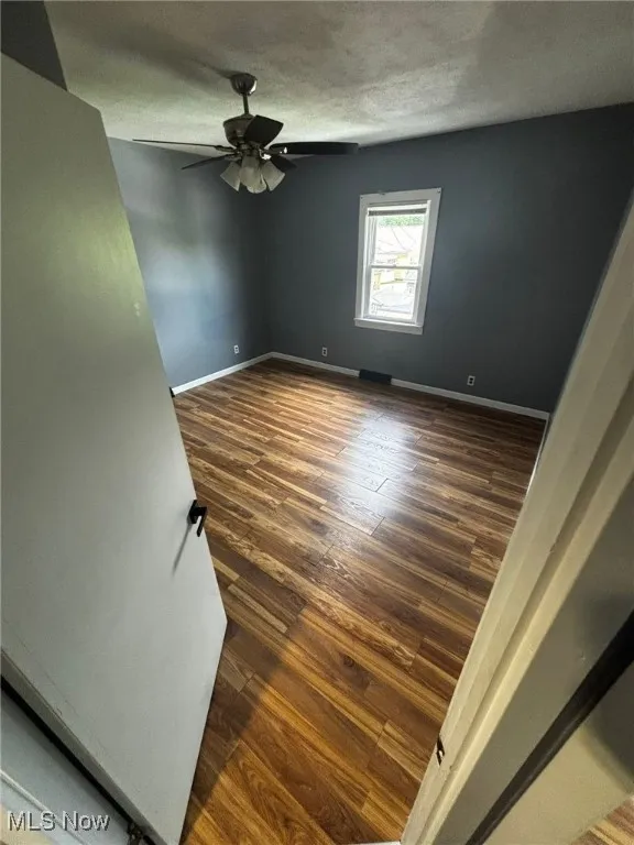 Empty room with a ceiling fan, dark wood-style flooring, and a textured ceiling