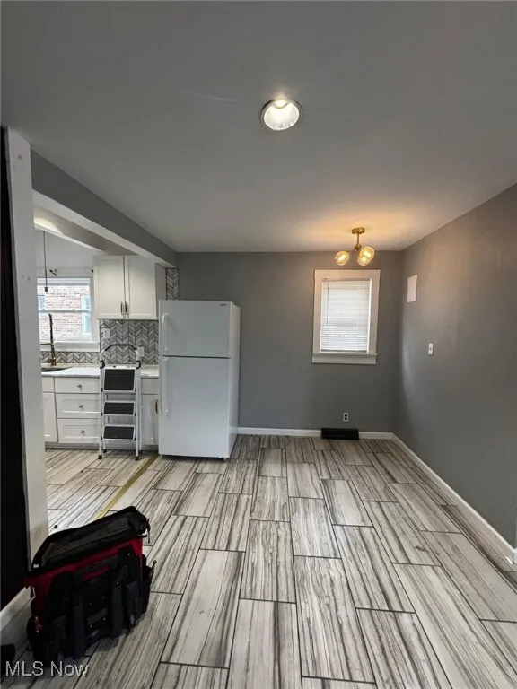 Kitchen with freestanding refrigerator, light countertops, wood finish floors, white cabinetry, and decorative backsplash