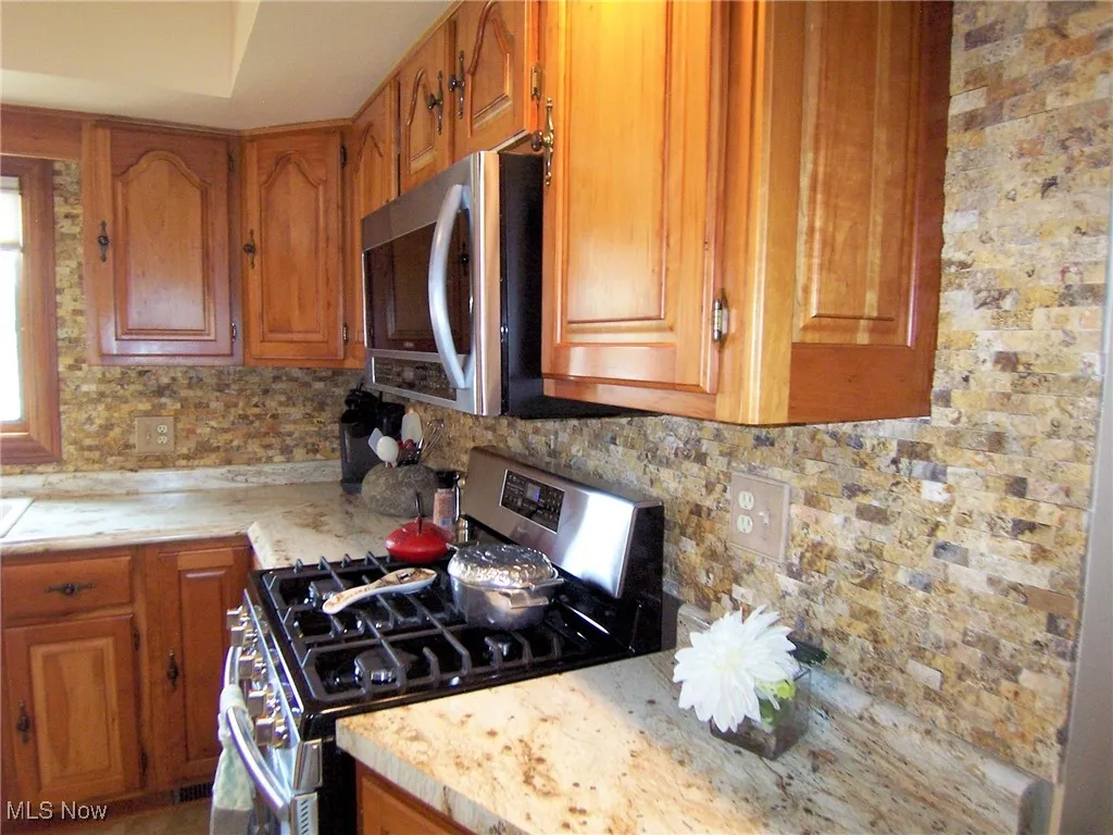 Kitchen featuring stainless steel appliances, brown cabinets, and decorative backsplash