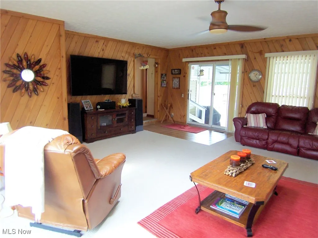 Carpeted living room featuring wood walls and a ceiling fan