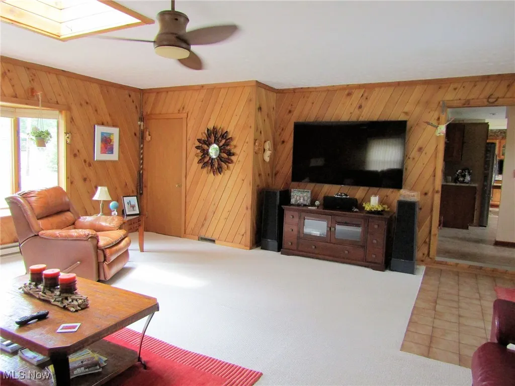 Carpeted living area with wooden walls, ceiling fan, and a skylight