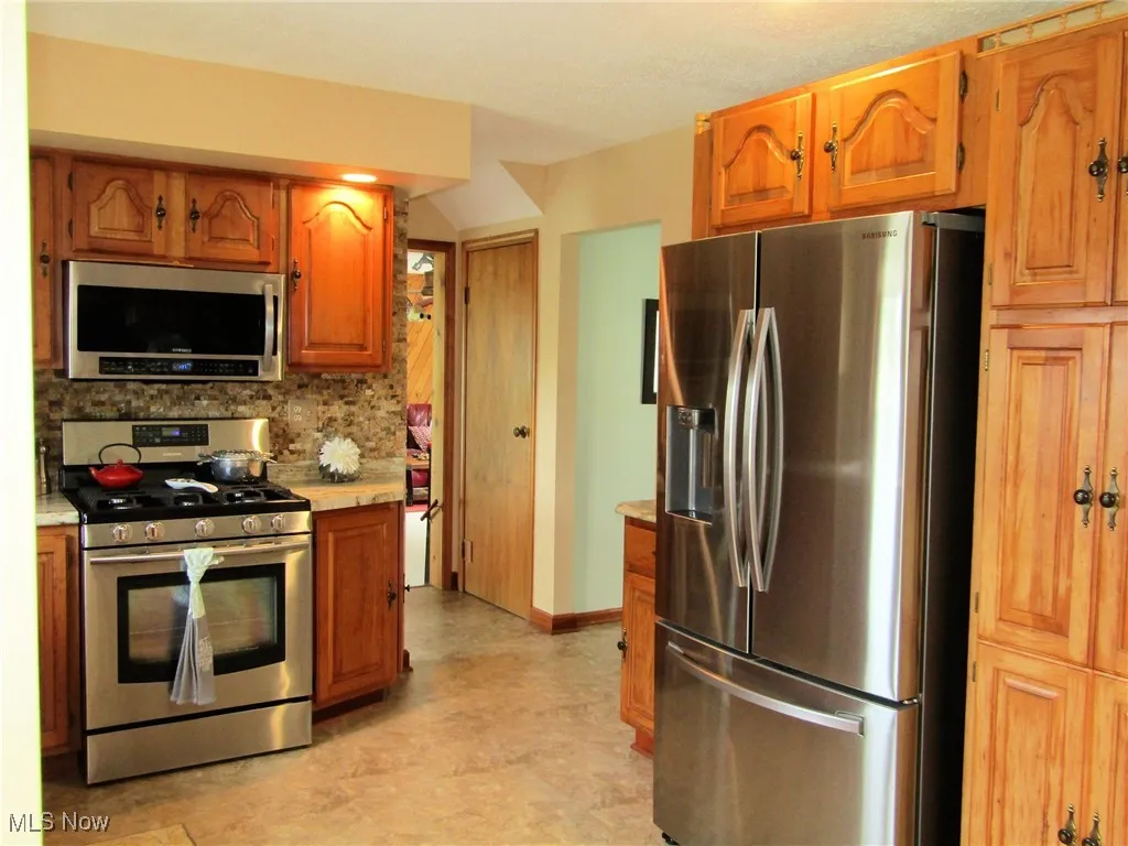 Kitchen featuring stainless steel appliances, light countertops, decorative backsplash, and brown cabinetry