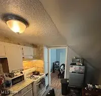 Kitchen with white gas stove, vaulted ceiling, light countertops, a textured ceiling, and white cabinetry