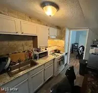 Kitchen with gray cabinets, light countertops, a textured ceiling, white cabinetry, and stainless steel microwave