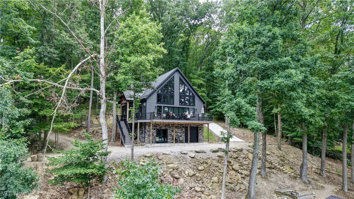 house with stairway, stone siding, a deck, and a wooded view