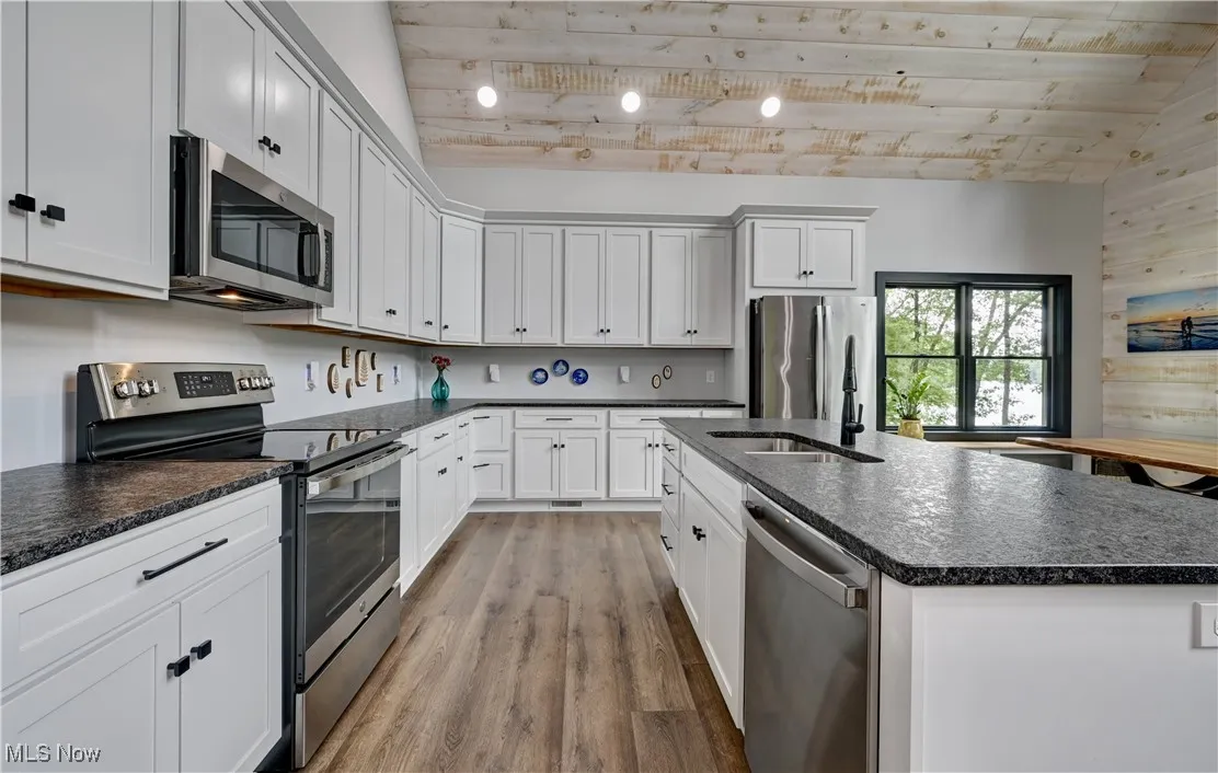 Kitchen with stainless steel appliances, light wood-type flooring, wood ceiling, lofted ceiling, and a kitchen island with sink