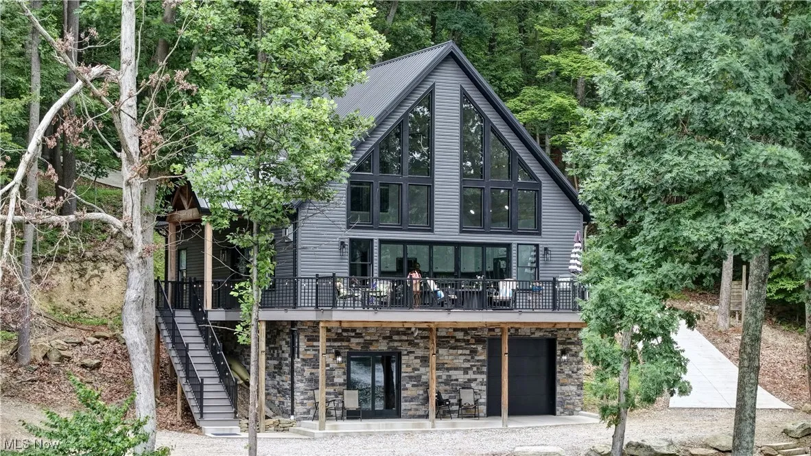 Front of structure with stone & vinyl siding, a deck, stairs, an attached garage, and driveway