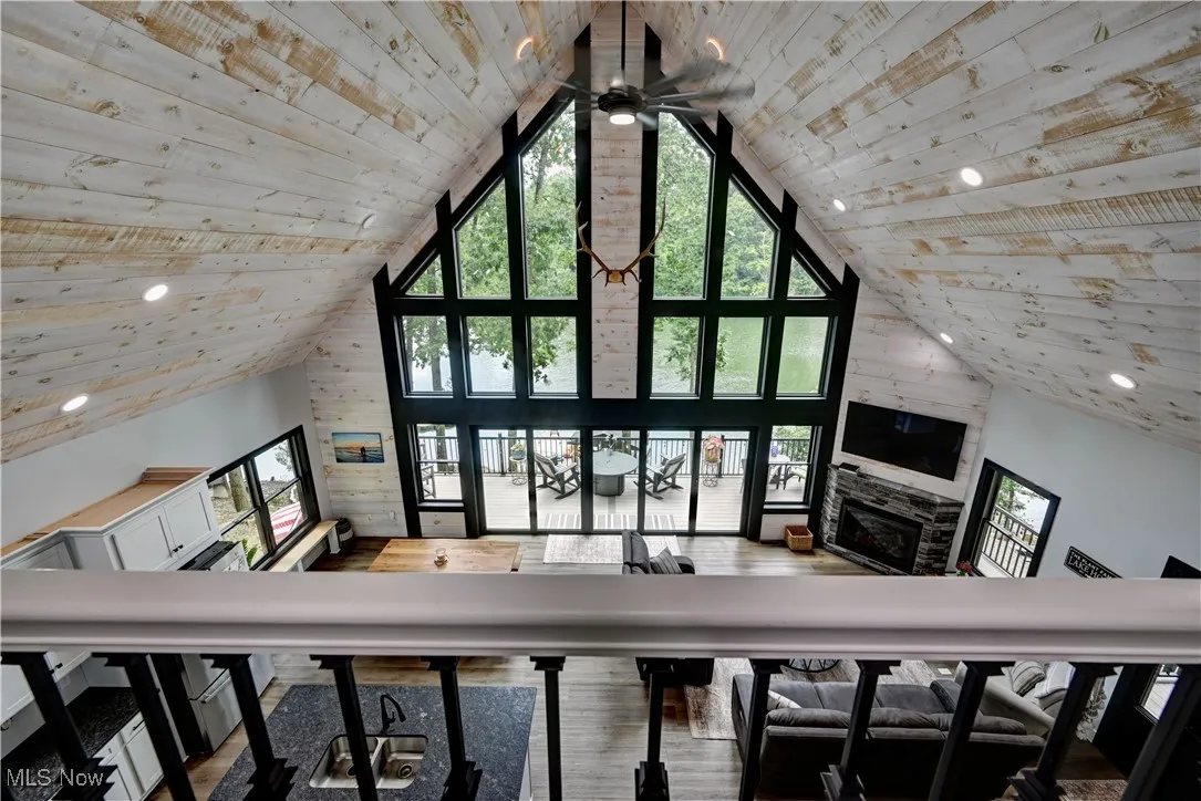 Loft view with high vaulted ceiling, wooden ceiling, a fireplace, ceiling fan, and wood finished floors