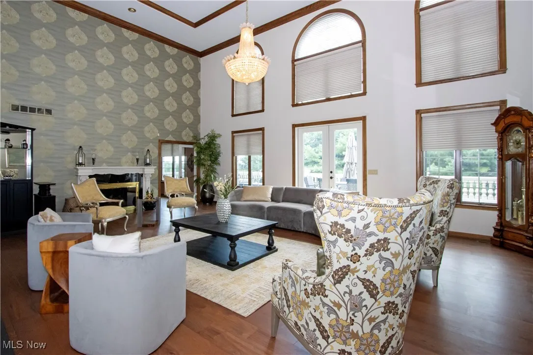 Living room featuring crown molding, wood finished floors, wallpapered walls, a premium fireplace, and a towering ceiling