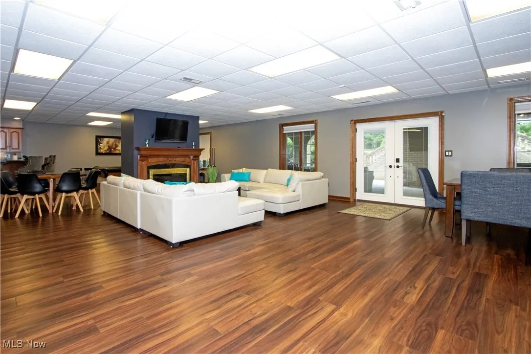 Living area with french doors, dark wood-type flooring, a drop ceiling, and a glass covered fireplace