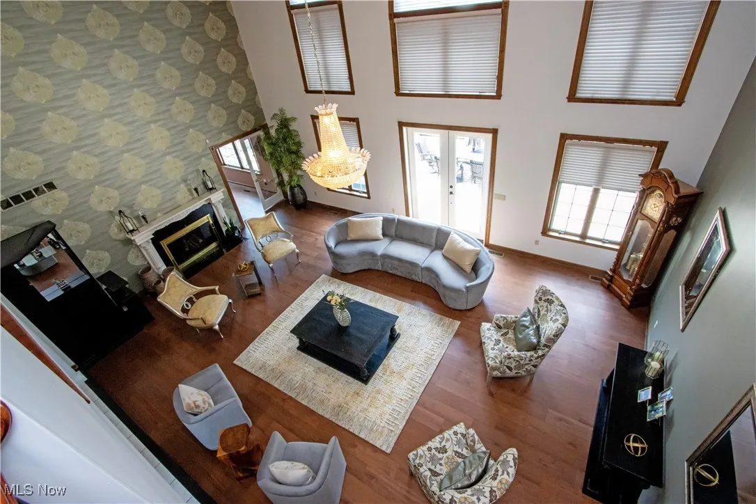 Living area featuring a towering ceiling, a glass covered fireplace, wallpapered walls, and wood finished floors