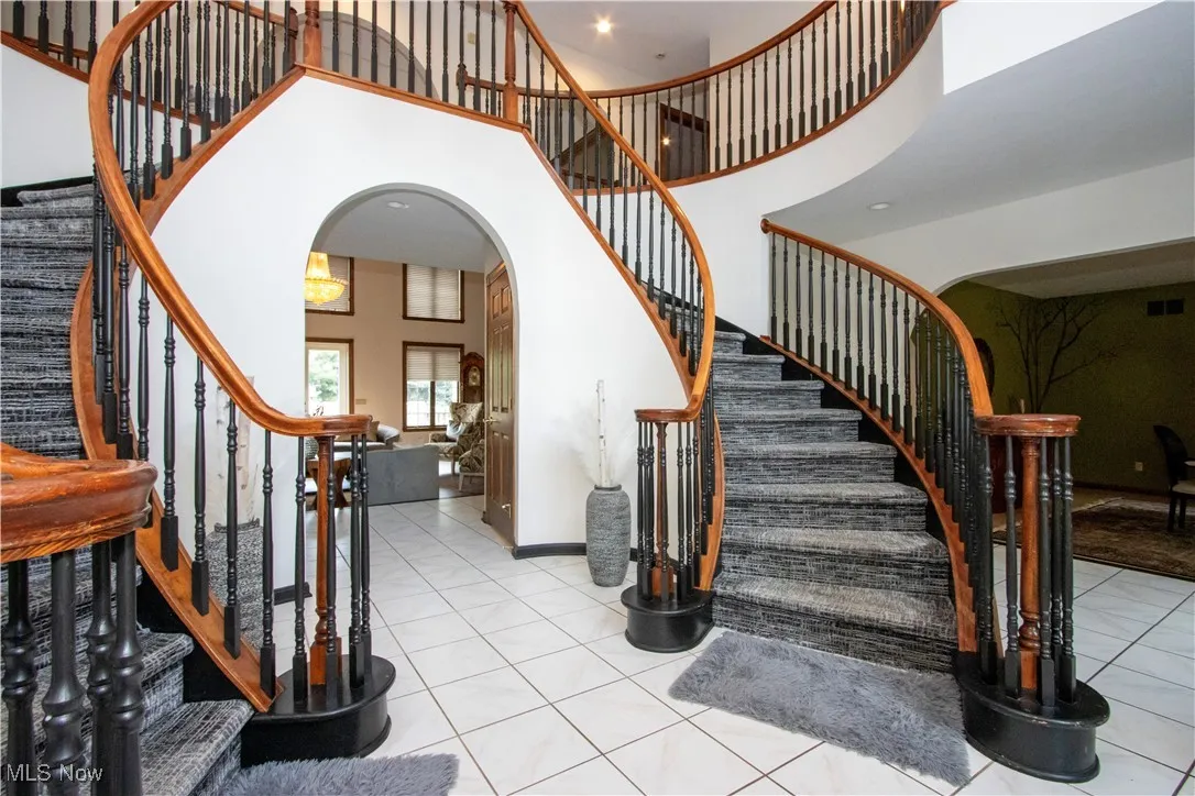 Staircase featuring arched walkways, a high ceiling, tile patterned flooring, and recessed lighting