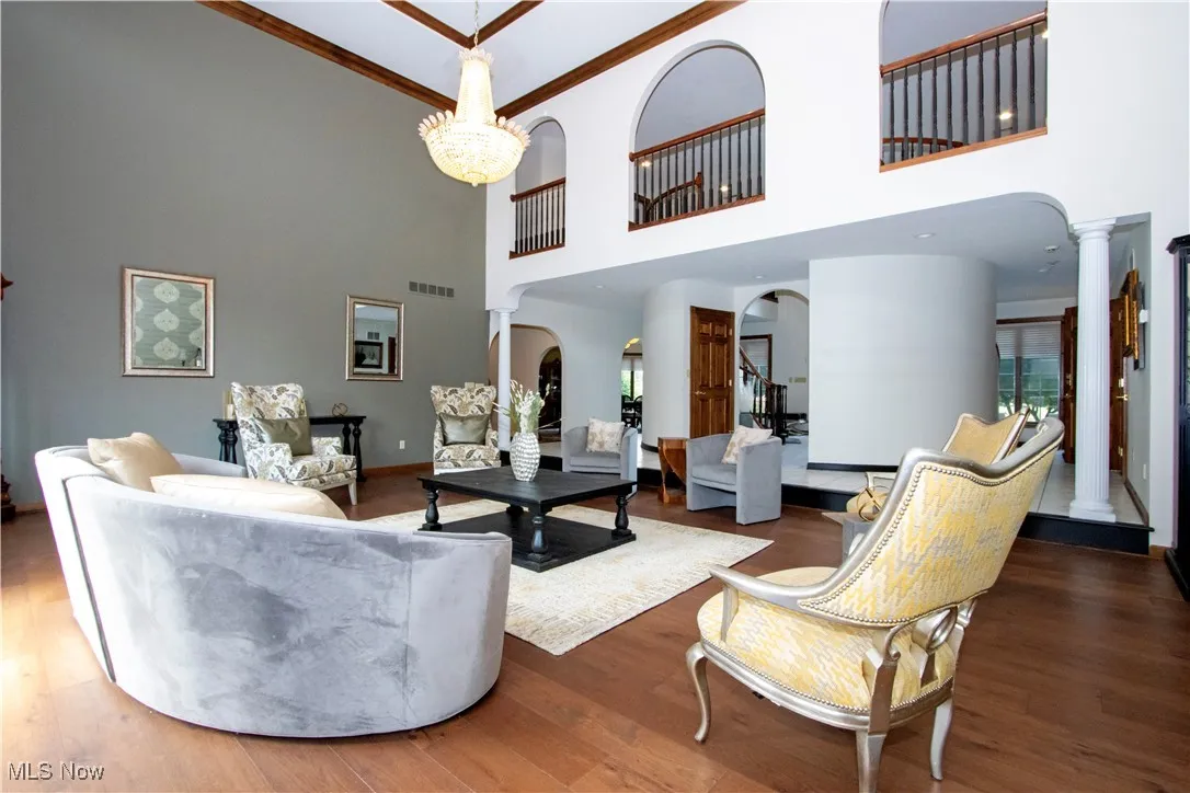 Living room with ornate columns, a high ceiling, wood finished floors, arched walkways, and crown molding