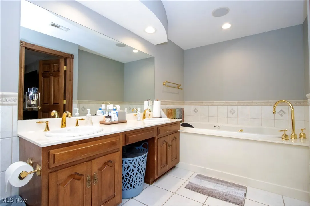 Bathroom with double vanity, tile patterned floors, a bath, a wainscoted wall, and tile walls