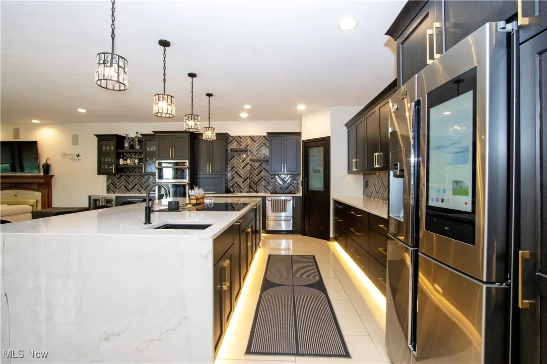 Kitchen with stainless steel appliances, backsplash, decorative light fixtures, light tile patterned flooring, and a large island