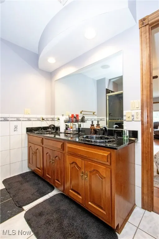 Full bath with double vanity, tile patterned flooring, tile walls, and wainscoting