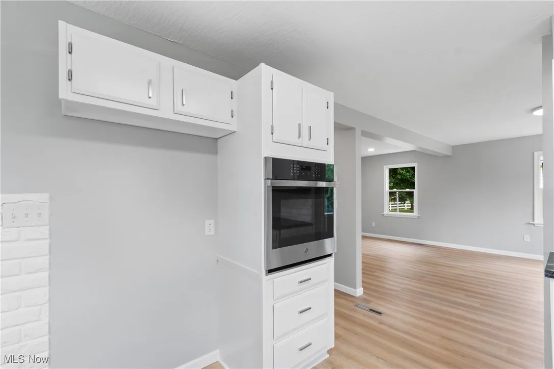Kitchen featuring stainless steel oven, white cabinets, open floor plan, light wood-style flooring, and recessed lighting
