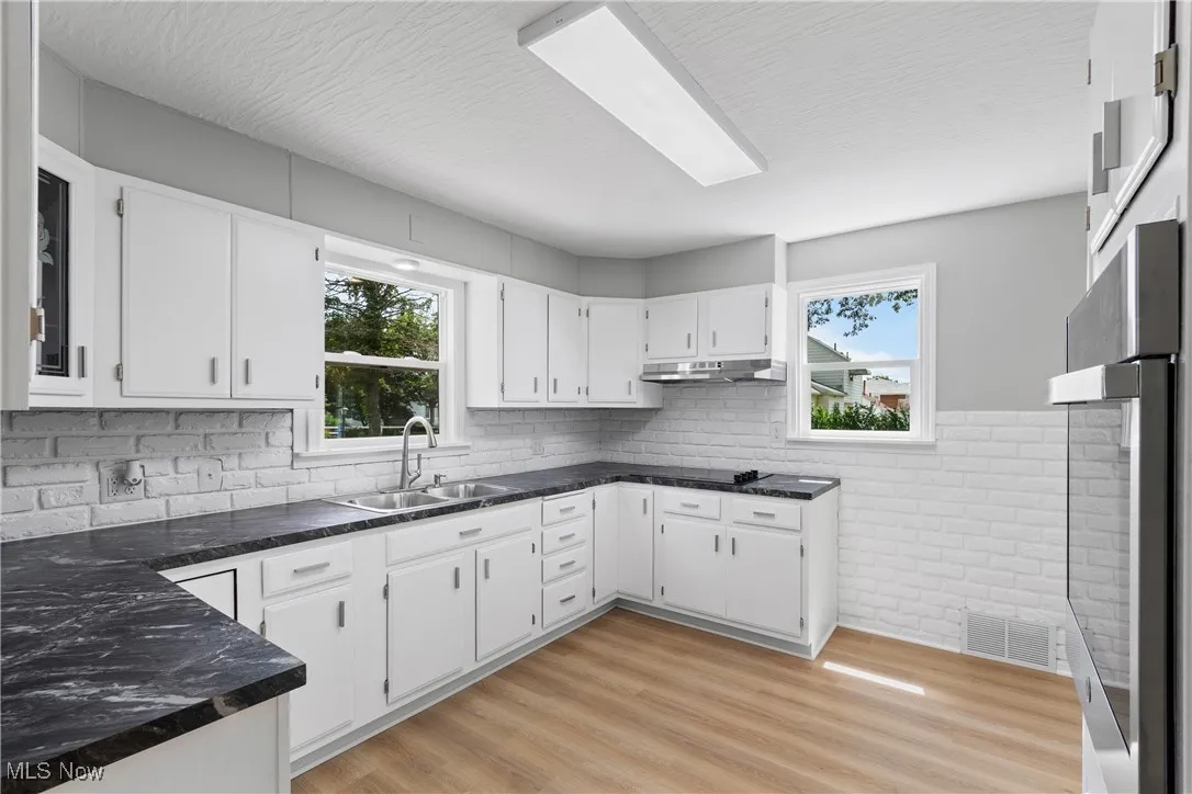 Kitchen with white cabinets, light wood-style floors, stainless steel oven, backsplash, and under cabinet range hood