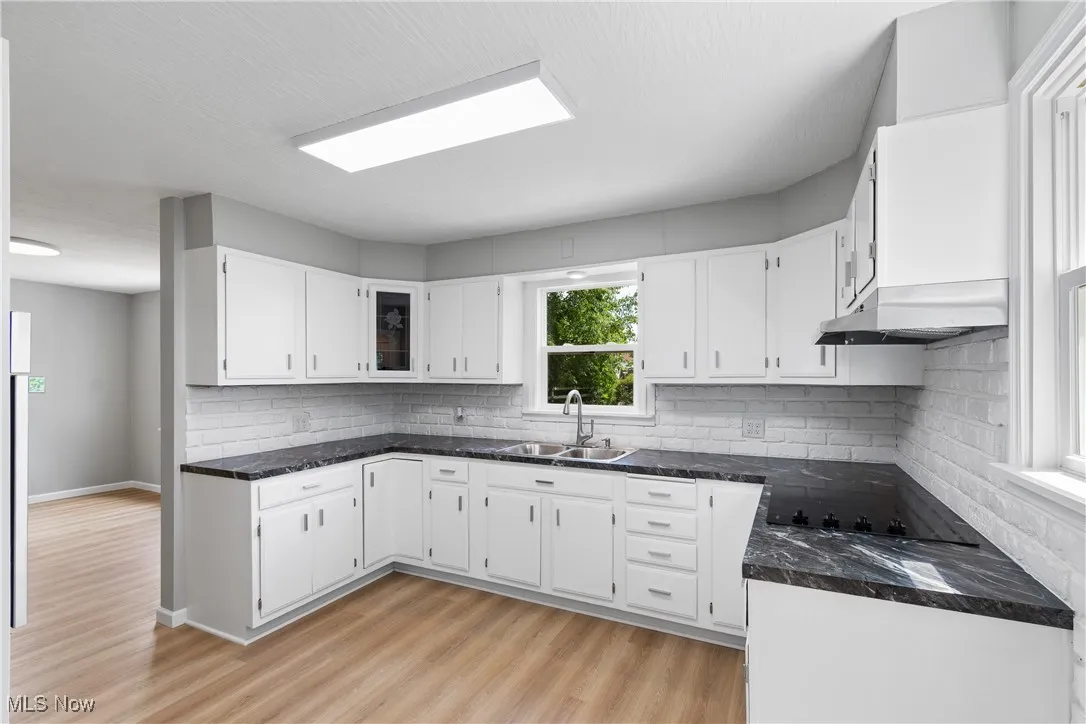Kitchen featuring white cabinets, tasteful backsplash, dark countertops, and light wood finished floors