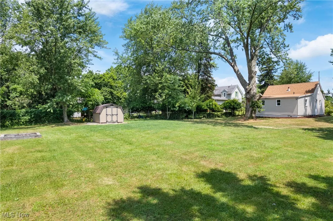 View of grassy yard featuring a storage unit and a fire pit