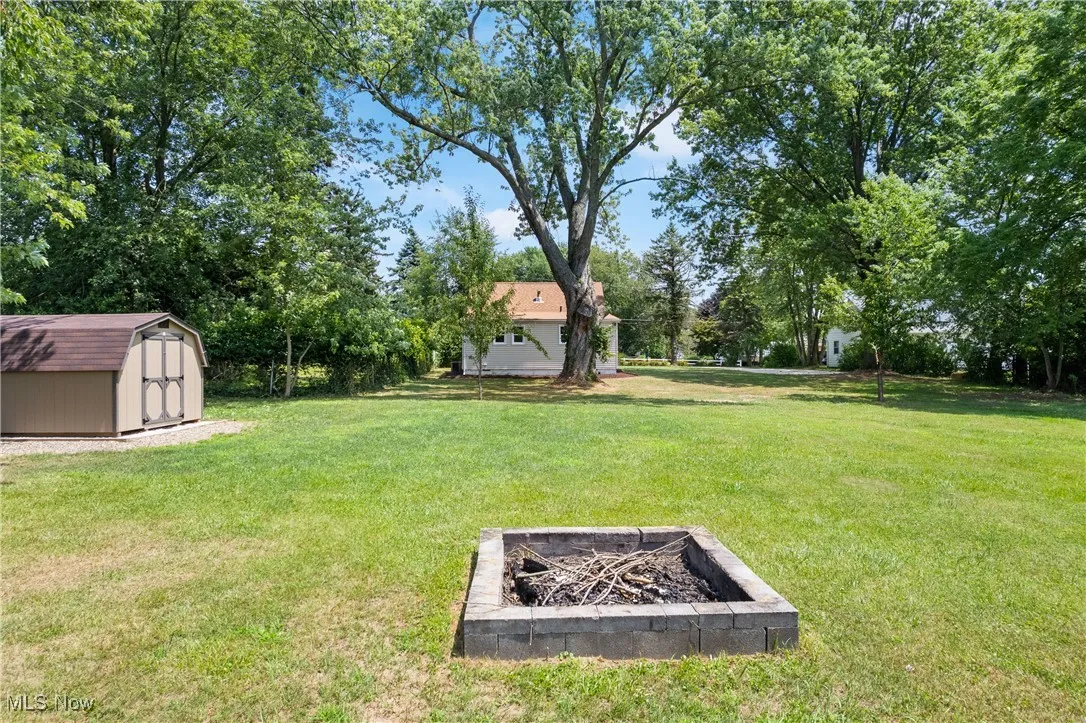 View of grassy yard featuring an outdoor fire pit, a shed, and view of wooded area