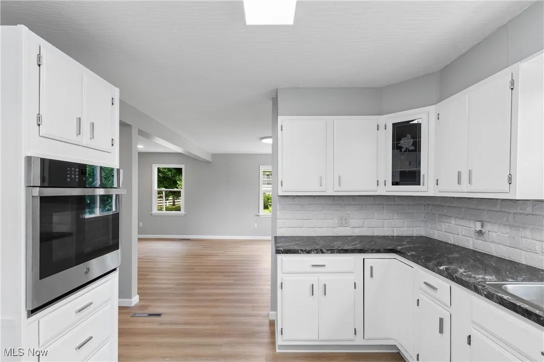 Kitchen with stainless steel oven, backsplash, light wood-type flooring, and white cabinetry
