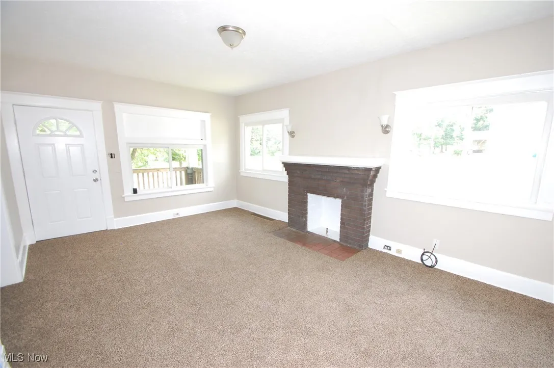 Unfurnished living room with carpet floors and a brick fireplace