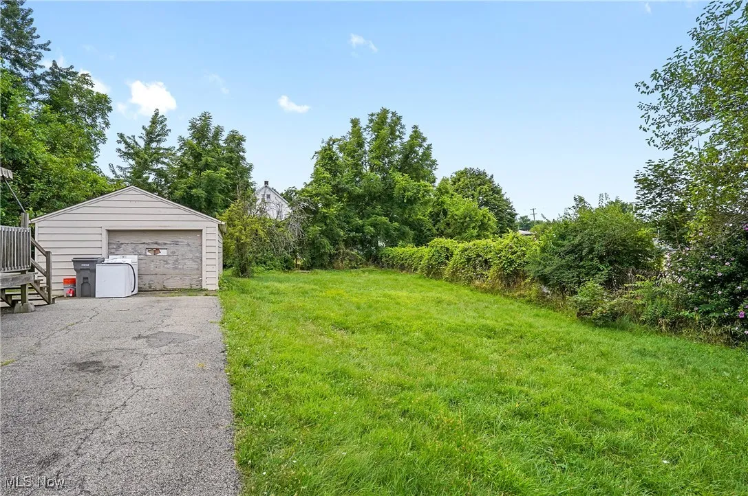 View of green lawn featuring an outbuilding, a garage, and driveway