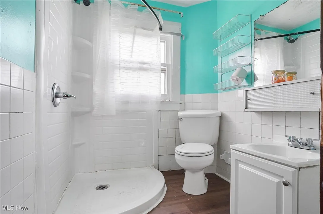 Bathroom featuring wood finished floors, tile walls, vanity, a shower, and wainscoting