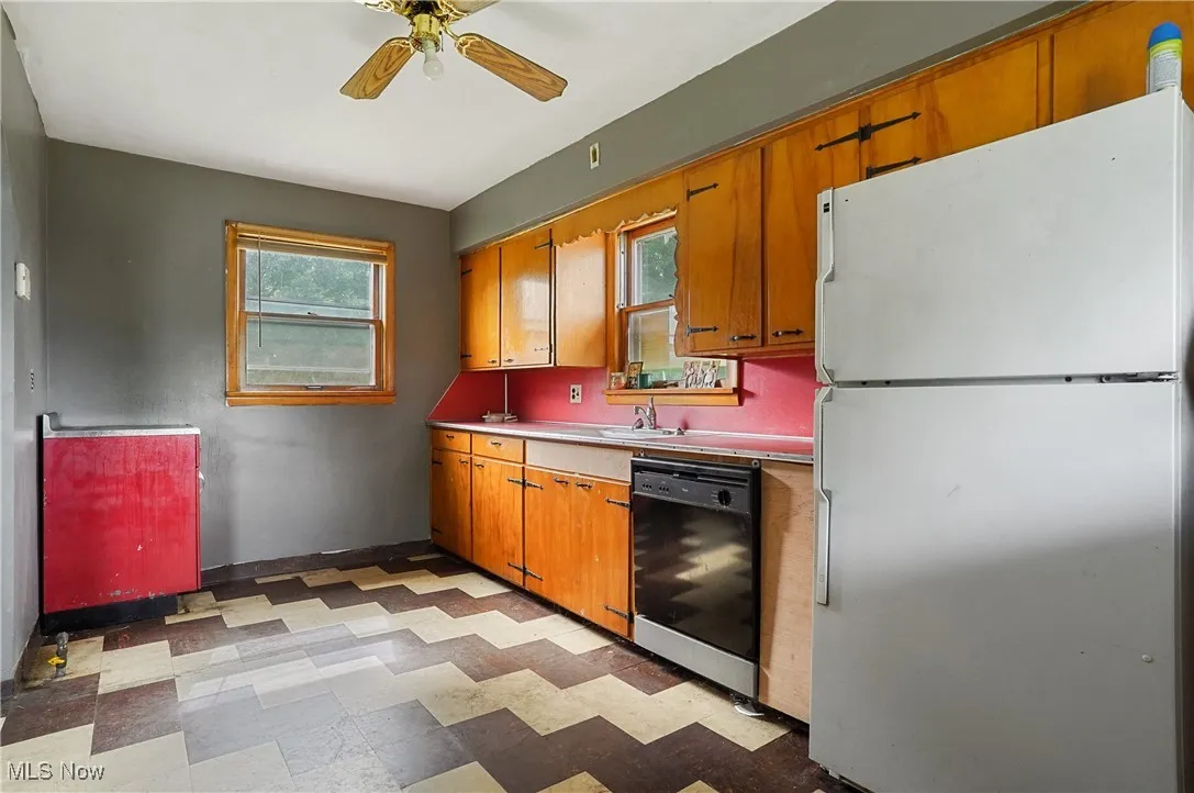 Kitchen with freestanding refrigerator, light flooring, a ceiling fan, black dishwasher, and brown cabinets
