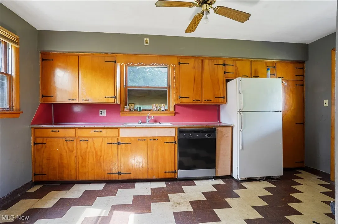 Kitchen with freestanding refrigerator, black dishwasher, tile patterned floors, ceiling fan, and brown cabinetry