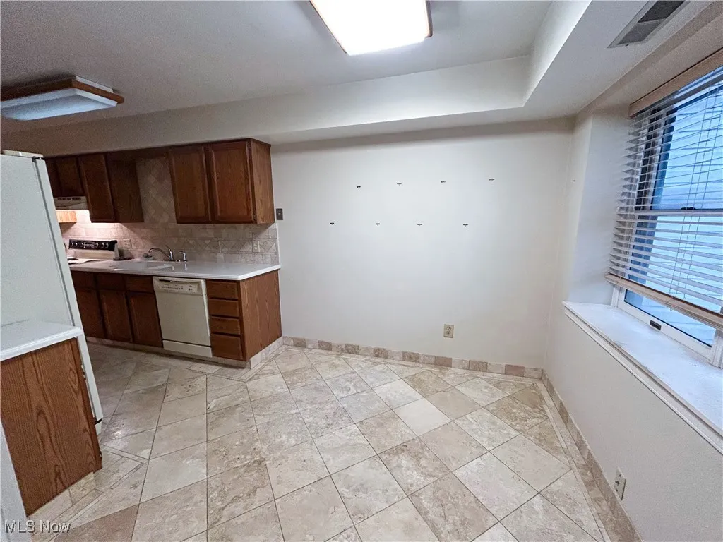 Kitchen featuring decorative backsplash, white appliances, and light countertops