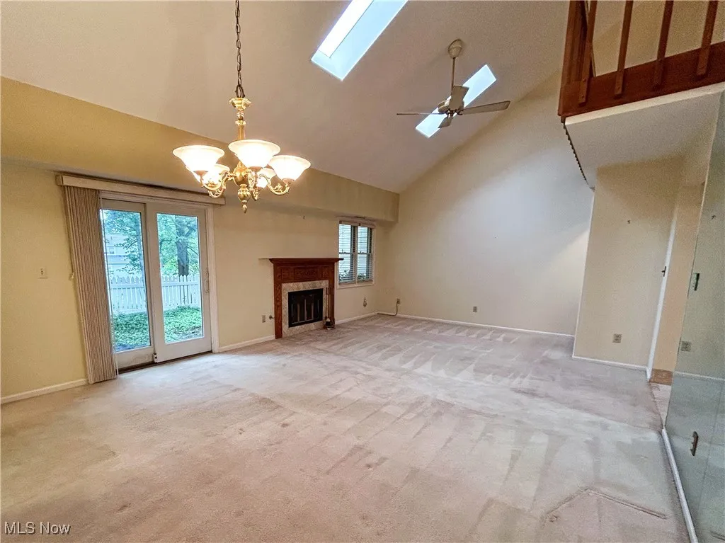 Living room featuring a fireplace, ceiling fan, a chandelier, a skylight, light carpet, windows, sliding door to backyard patio, and a high vaulted ceiling
