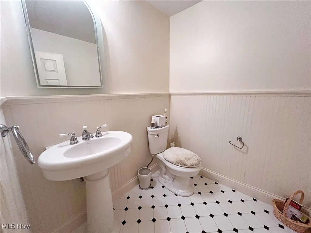 First floor half bath featuring toilet, sink, a wainscoted wall and tile patterned floors