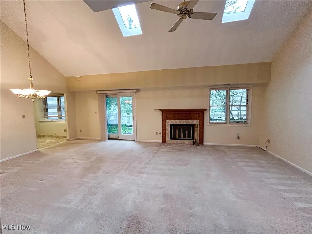 Living room featuring a fireplace, ceiling fan, a chandelier, a skylight, light carpet, windows, sliding door to backyard patio, and a high vaulted ceiling