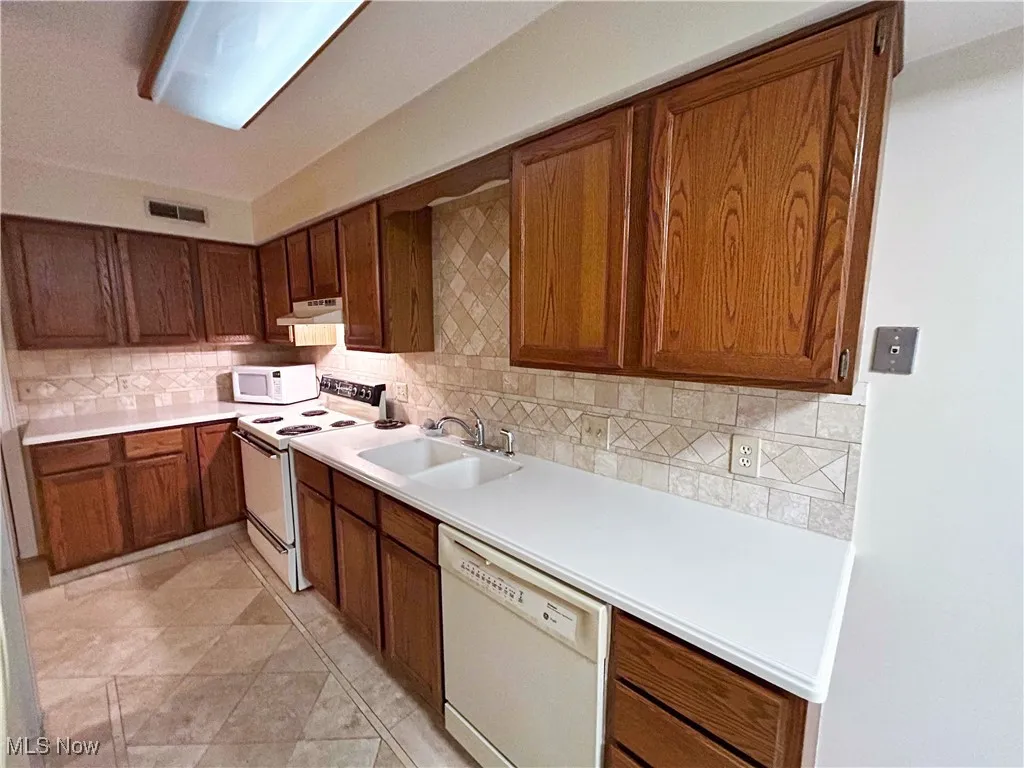 Kitchen with white appliances, tasteful backsplash, brown cabinets, and light countertops