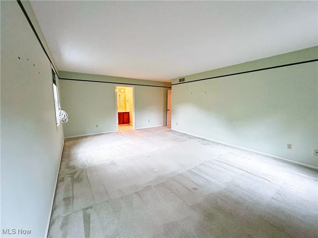 Carpeted master bedroom featuring window and view of full bath