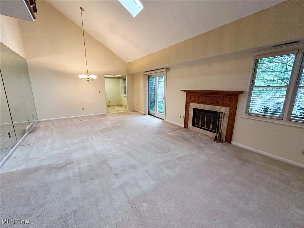 Living room featuring a fireplace, a chandelier, view of dining area, a skylight, light carpet, windows, sliding door to backyard patio, and a high vaulted ceiling