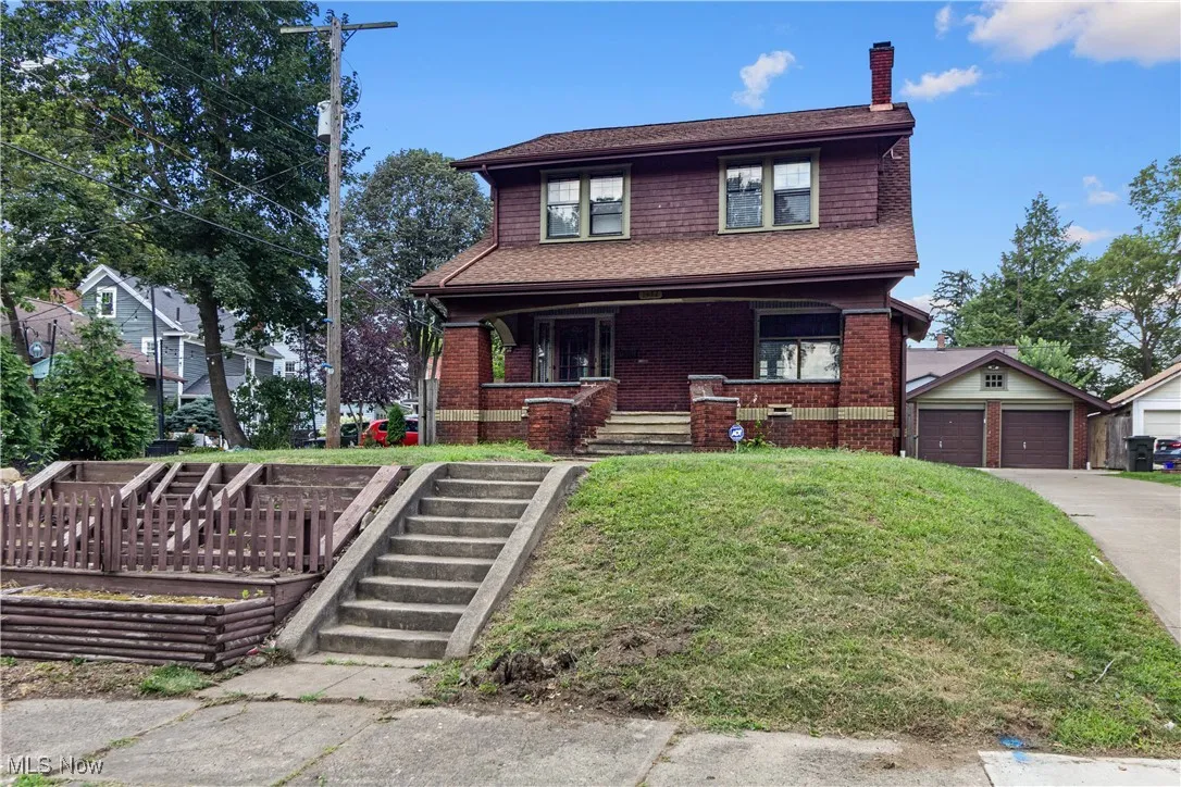 View of front of home with a chimney, a front yard, a detached garage, a porch, and an outdoor structure