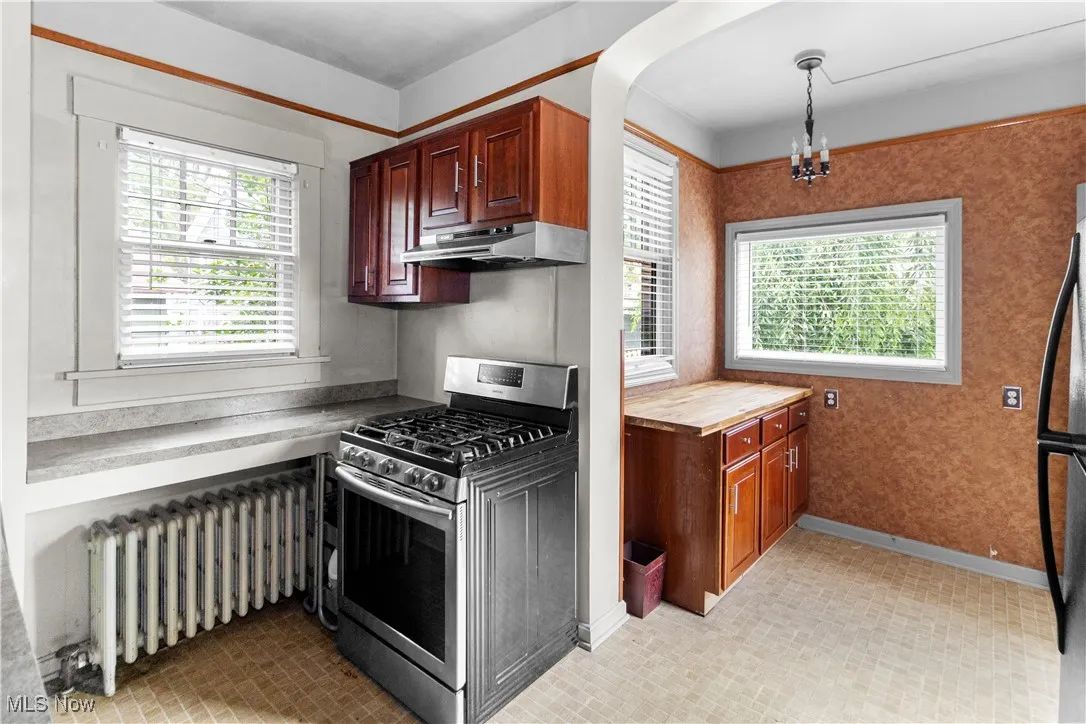 Kitchen with stainless steel gas range, radiator, a chandelier, and healthy amount of natural light