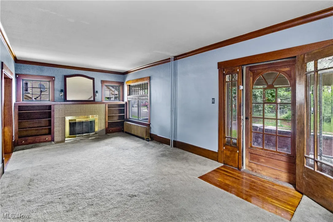 Unfurnished living room featuring crown molding, radiator, carpet floors, a fireplace with flush hearth, and built in shelves