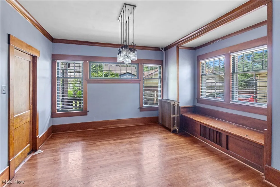 Unfurnished dining area with ornamental molding, wood finished floors, a chandelier, radiator, and plenty of natural light