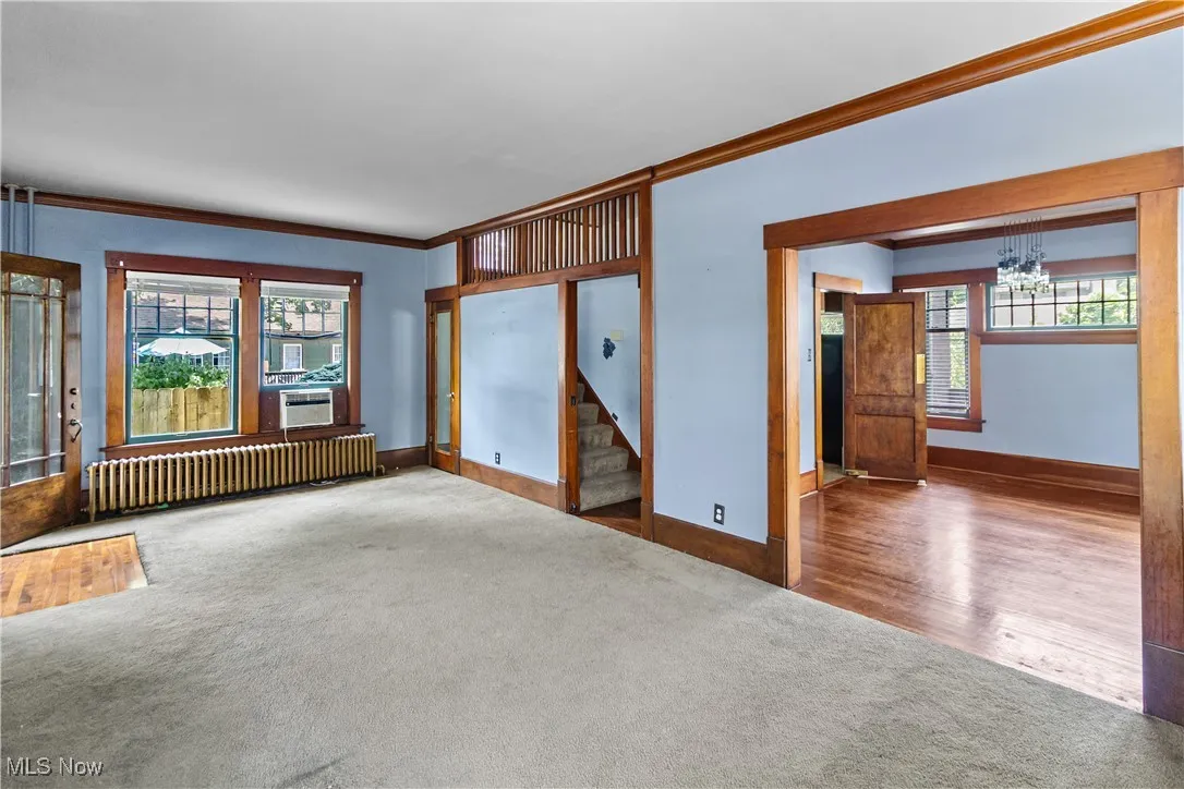 Empty room featuring ornamental molding, carpet floors, radiator heating unit, a chandelier, and stairs