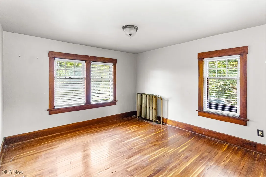 Unfurnished room featuring hardwood / wood-style flooring, healthy amount of natural light, and radiator heating unit
