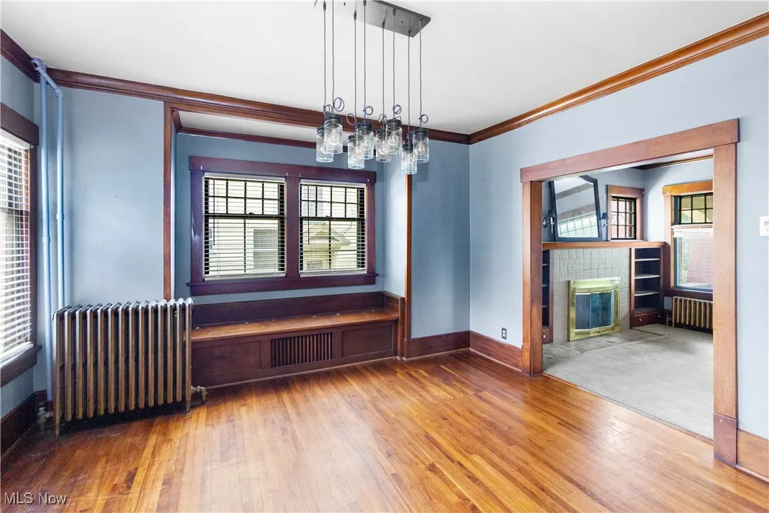 Unfurnished dining area featuring radiator heating unit, a tiled fireplace, wood finished floors, and ornamental molding