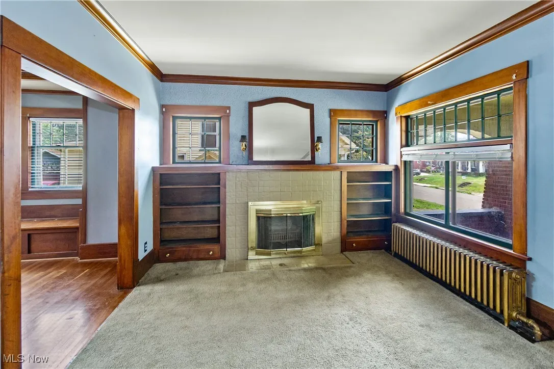 Unfurnished living room with crown molding, radiator, a fireplace with flush hearth, and wood finished floors
