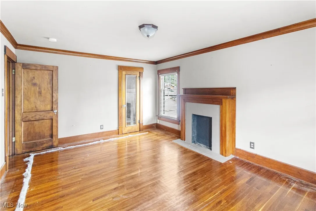 Unfurnished living room with wood finished floors, crown molding, and a fireplace with flush hearth