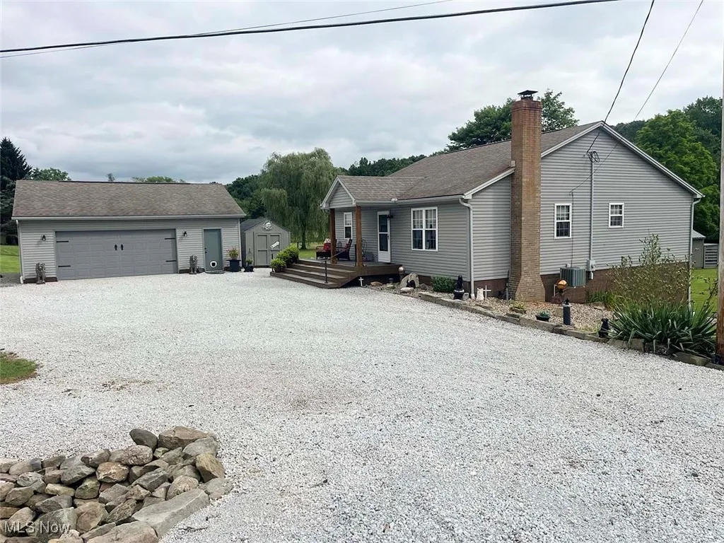 Single story home featuring driveway, a shed, a chimney, a deck, and a shingled roof