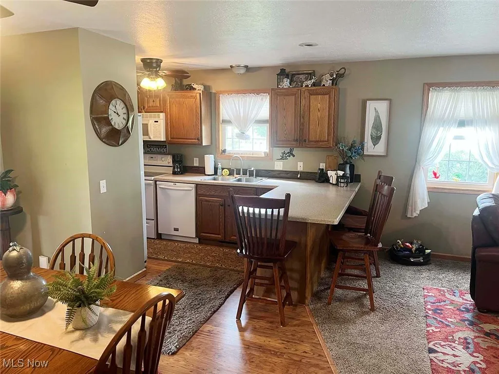Kitchen with a ceiling fan, a breakfast bar area, white appliances, brown cabinetry, and a peninsula